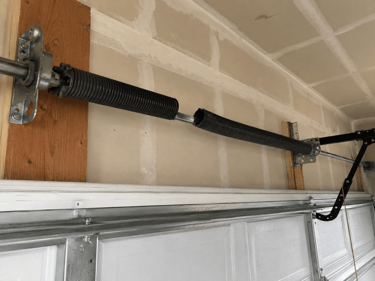 Before spring replacement showing a broken torsion spring above a residential garage door in Tehaleh.